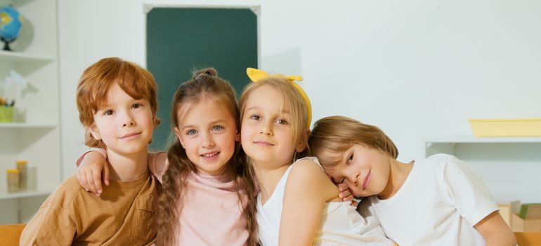 4 children sitting and hugging in a classroom