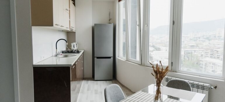 Bright modern kitchen with a glass table, minimalist design, and cityscape view through large windows.