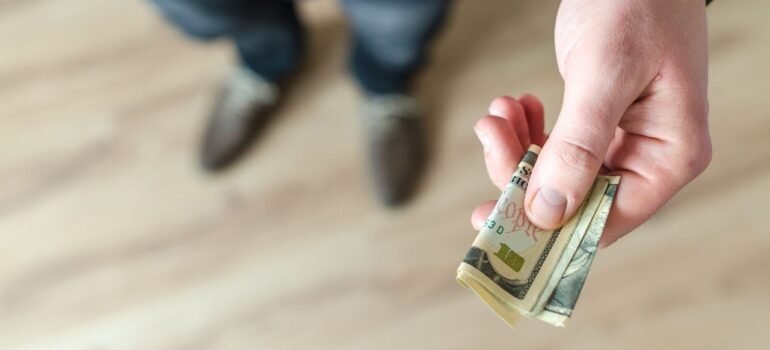 A close-up of a man's hand holding rolled US dollar bills, offering cash after learning about how much to tip movers Bay Area