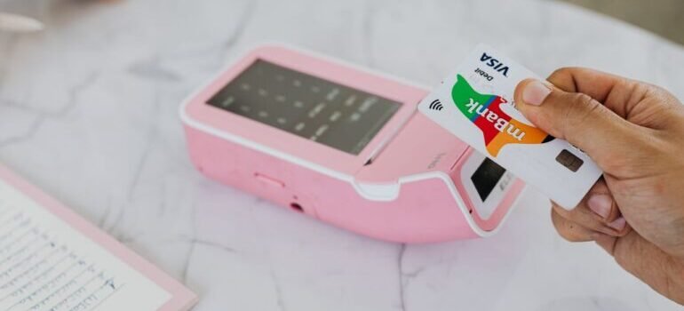 Hand using a contactless card on a pink POS terminal for a wireless transaction.