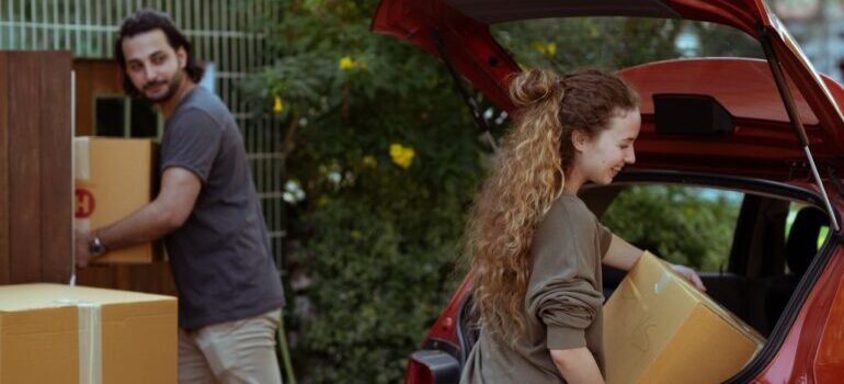 A cheerful young couple unloading boxes from a car trunk into their new home in the countryside.