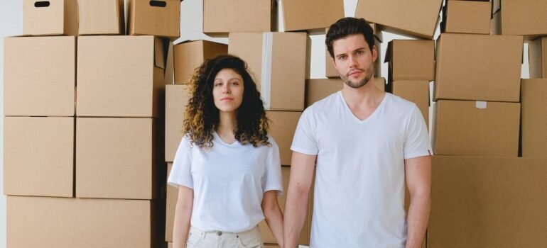 A young couple holding hands in front of a stack of cardboard boxes,