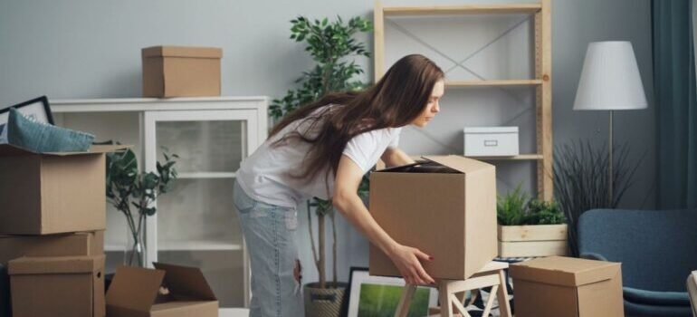 A young woman with long hair arranging boxes in her new home, after learning about what will movers not move